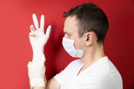 Professional medic in protective mask on face putting on blue latex gloves on hands. Young man surgeon in face mask wearing sterile medical glove. Medical examination in hospital. Coronavirus COVID-19の写真素材