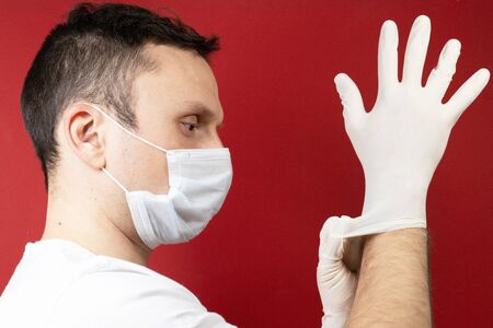 Professional medic in protective mask on face putting on blue latex gloves on hands. Young man surgeon in face mask wearing sterile medical glove. Medical examination in hospital. Coronavirus COVID-19の写真素材