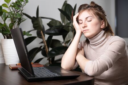 A tired woman searches for information in a laptop on the line in a Desk in the home room. Work at home. Chronic fatigue, lack of energy. Home quarantineの写真素材