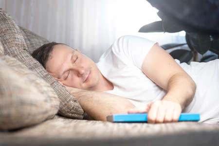 Beautiful young guy fell asleep on the sofa in the living room, he was reading a book. Rest, relaxationの写真素材