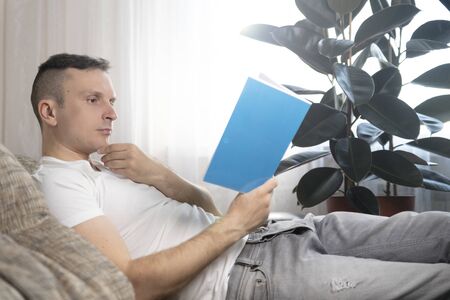 Leisure, education and the main concept-a smiling guy reads a book and sits at home on the couch. Rest, relaxation.の写真素材