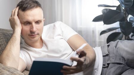 Leisure, education and the main concept-a smiling guy reads a book and sits at home on the couch. Rest, relaxation.の写真素材