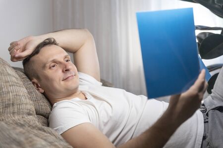 Leisure, education and the main concept-a smiling guy reads a book and sits at home on the couch. Rest, relaxation.の写真素材