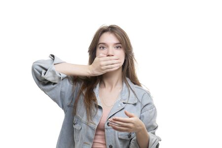 Portrait of a scared teenage girl looking surprised, shocked with a hand covering her mouth, someone gagging her, isolated white background. Human emotions, facial expressions, feelings, body language, reactionの写真素材