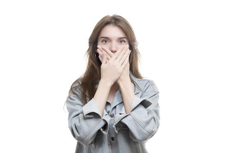 Portrait of a scared teenage girl looking surprised, shocked with a hand covering her mouth, someone gagging her, isolated white background. Human emotions, facial expressions, feelings, body language, reactionの写真素材