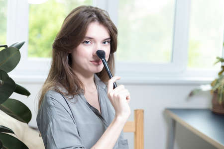 A beautiful girl is sitting in a bright room and making a selfie video for a fashion blog. The woman keeps a blog online and makes a photo. Fashion cosmetics reviewerの写真素材