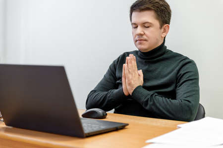 Relaxed corporate man sitting with closed eyes contemplating at work desk with laptop in office. Guy relaxing, relieves stress, gets positive thinking with yoga exercise. Stress free workplace conceptの写真素材