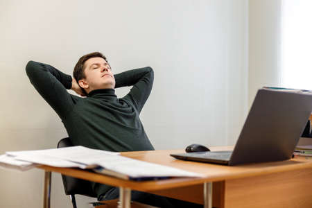 Relaxed corporate man sitting with closed eyes contemplating at work desk with laptop in office. Guy relaxing, relieves stress, gets positive thinking with yoga exercise. Stress free workplace conceptの写真素材