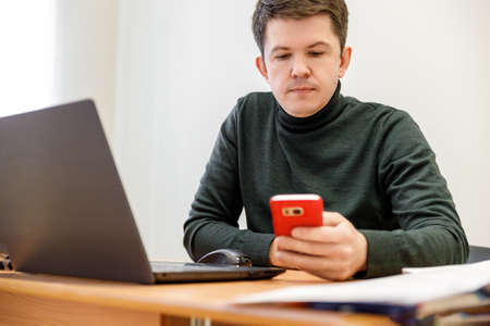 A close-up of a cute businessman or employer working on a digital tablet and talking on his smartphone in a modern office interior, a flash of light. The concept of conversation.の写真素材