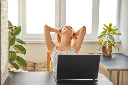 Portrait of an attractive woman on a chair at a table with a laptop, home office, remote work. Relax. The concept of work and rest. Concept photoの写真素材