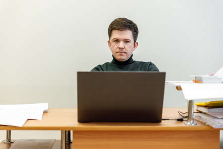 A casual businessman works in an office, sits at a Desk, types on a keyboard, looks at a computer screen. Concept of office work.の写真素材