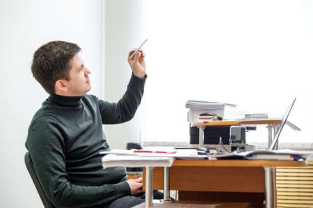 A casual businessman works in an office, sits at a Desk, types on a keyboard, looks at a computer screen. Concept of office work.の写真素材