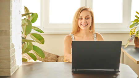 A woman in home clothes works on a computer in front of a monitor in a home atmosphere. Flexible working hours and remote work.の写真素材