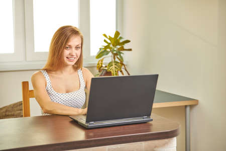 A woman in home clothes works on a computer in front of a monitor in a home atmosphere. Flexible working hours and remote work.の写真素材
