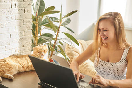 Funny girl professional laughter sitting with a laptop on a home office Desk, positive European woman fun to enjoy sincere emotions laughter study work on a PC. Quarantine, remote work.の写真素材