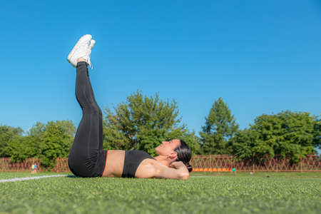 fitness, sports, exercises, training and the concept of people-a girl does an exercise on the triceps, legs and abs on the city sports field. The concept of a healthy lifestyleの写真素材