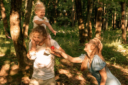 Happy family in the Park at sunset. Summer picnic. The concept of a healthy family. Mom, dad, daughter. Weekend in nature.の写真素材