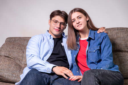 Young couple relaxing on the sofa smiling at the camera at home in the living roomの写真素材