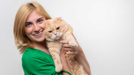 Studio portrait of an attractive woman with braces holding a cat in her hands, isolated on a white backgroundの写真素材
