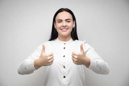 Happy Pretty young woman with long chestnut hair, Smiling and showing thumb up, dressed in casual clothes. I like that. Good job.Human emotions concept. Copy space for your textの写真素材