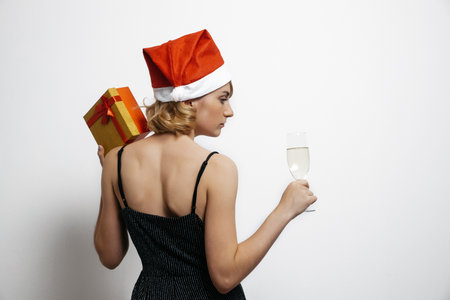 The view from the back. A woman in a beautiful black dress holds a glass of champagne and a gift in her hand. Holiday, new year, corporate eventの写真素材