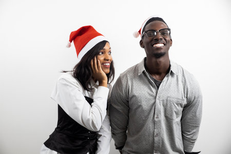 Portrait of a cheerful young African couple wearing Christmas hats, hugging, isolated on a light backgroundの写真素材