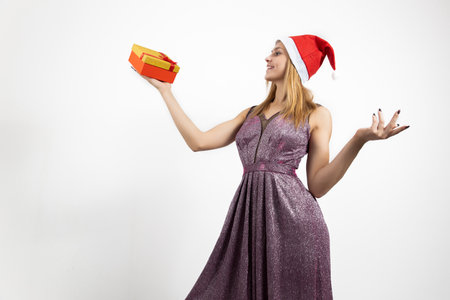 A beautiful girl standing on a white background with gifts in her hands, smiling a beautiful smile. Celebrating Christmas in the office or New year's eveの写真素材