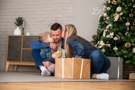 Mom and son kiss dad and husband. Merry Christmas and happy holidays mom, dad and son sorting gifts. A loving family enjoys the new year's moodの写真素材