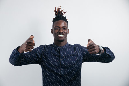 Portrait of a cheerful, positive, handsome man with black skin, a beaming smile in a shirt, giving a thumbs up with a finger to the camera, isolated on a gray backgroundの写真素材