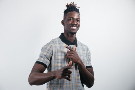 Portrait of a cheerful, positive, handsome man with black skin, a beaming smile in a shirt, giving a thumbs up with a finger to the camera, isolated on a gray backgroundの写真素材