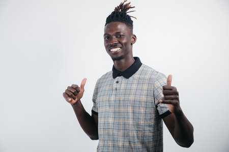 Portrait of a cheerful, positive, handsome man with black skin, a beaming smile in a shirt, giving a thumbs up with a finger to the camera, isolated on a gray backgroundの写真素材