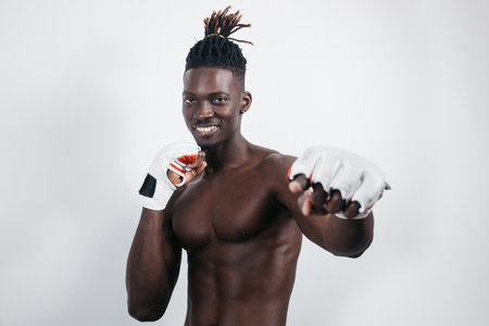 A confident young African boxer in boxing gloves reaches out and stares into the camera while standing isolated on the greyの写真素材