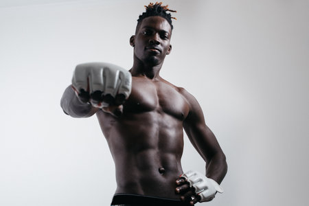 A confident young African boxer in boxing gloves reaches out and stares into the camera while standing isolated on the greyの写真素材