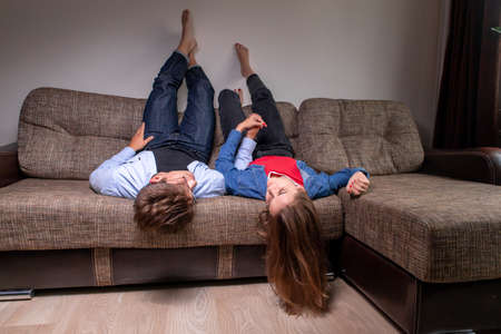 Happy young romantic couple relax with feet up on cosy sofa at home holding hands dreaming togetherの写真素材