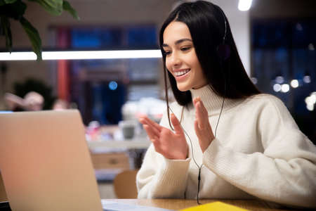 Smiling young female in headphones with laptop applaud watching webinar or communicate by conference video callの写真素材