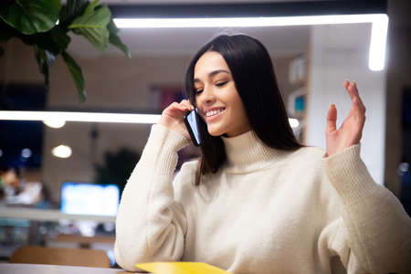 Happy young girl talking on phone enjoying mobile conversation, speaking, making business call in officeの写真素材