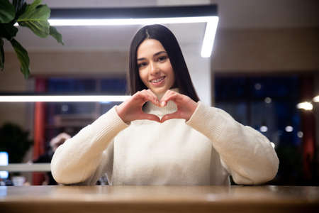 Smiling thankful young european female blogger showing heart love hand gesture, charity conceptの写真素材