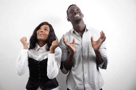 Smiling young african american couple looking up having fun celebrate success together on white studio backgroundの写真素材