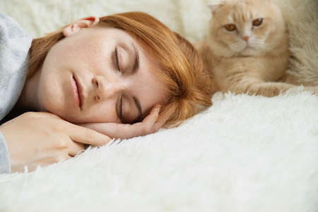 Close up pretty young red-haired female with ginger pet cat lying on bed sleeping relax in comfy bedの写真素材