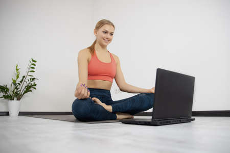 Athletic young female in comfortable stylish sportswear watching yoga class online on laptop on fitness carpetの写真素材