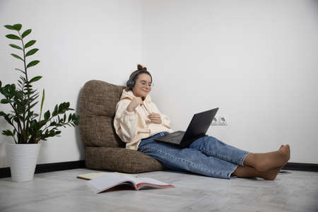 Smiling teenage school student in wireless headphones studying online with laptop at home. Remote education conceptの写真素材