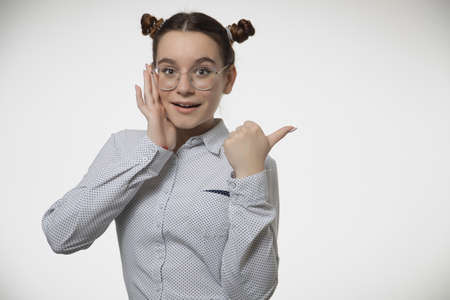 Happy young female teen in stylish modern glasses pointing finger aside at copy space for ad on white studio backgroundの写真素材