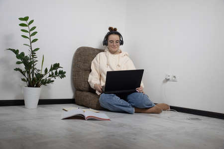 Smiling teenage school student in wireless headphones studying online with laptop. Young girl in earphones doing homework learning with computer at home, prepare for exam. Remote education concept.の写真素材