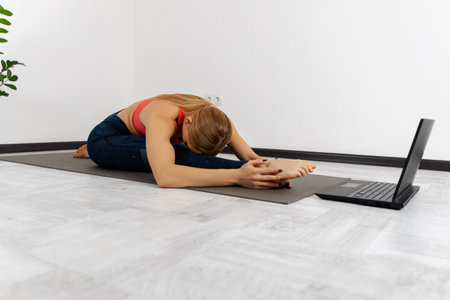 Top view of a fit, athletic, healthy woman sitting on a mat in a yoga pose, doing breathing exercises, watching online yoga classes on a laptop. Online training, personal training, coach teaches online via video linkの写真素材