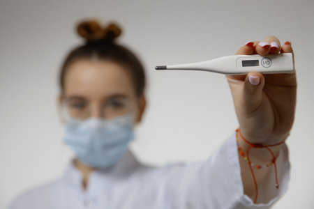 Close-up of a picture of a doctor in a protective mask, ready to use a thermometer (thermometer - gun) to check the body temperature for the presence of virus symptoms - the concept of an epidemic outbreak of the virusの写真素材