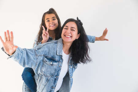 Happy child girl daughter piggyback on smiling mother. Stylish mum, kid having fun together. Two female generationsの写真素材