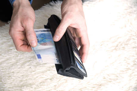 Close up male hands with empty wallet taking out last cash money euros. Man holding currency remains and purse. Bankruptcy economic financial, income decline, poverty, unemployment concept, top view.の写真素材