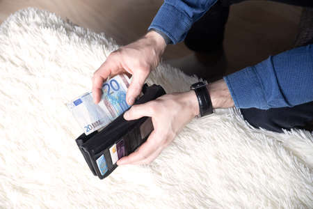 Close up male hands with empty wallet taking out last cash money euros. Man holding currency remains and purse. Bankruptcy economic financial, income decline, poverty, unemployment concept, top view.の写真素材