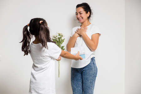 Cute child girl congratulating loving mum, giving bouquet of white flowers, gift box. Womens or Mothers Dayの写真素材