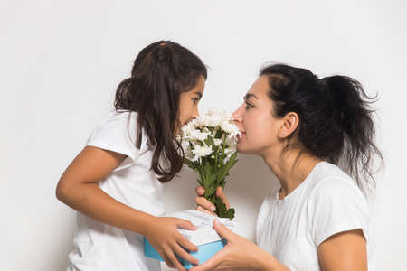 Cute child girl congratulating loving mum, giving bouquet of white flowers, gift box. Womens or Mothers Dayの写真素材